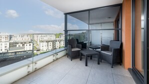 Un balcón con vistas a la ciudad, amueblado con una silla, una mesita y un sofá.