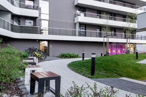 A modern apartment building with balconies, a paved pathway, and a small garden area.