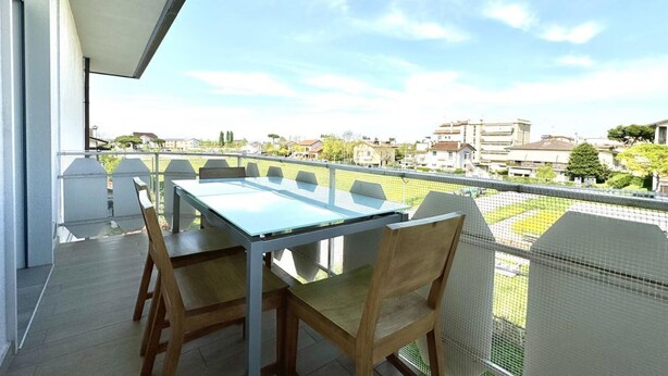 Un balcon avec une table et des chaises, donnant sur un quartier résidentiel avec des maisons et de la verdure.