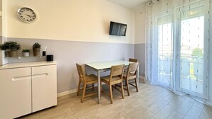 Une petite cuisine avec une table à manger, des chaises, une horloge, un téléviseur et une porte-fenêtre coulissante.
