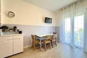 Una cocina pequeña con una mesa de comedor, sillas, un reloj, un televisor y un ventanal corredero.