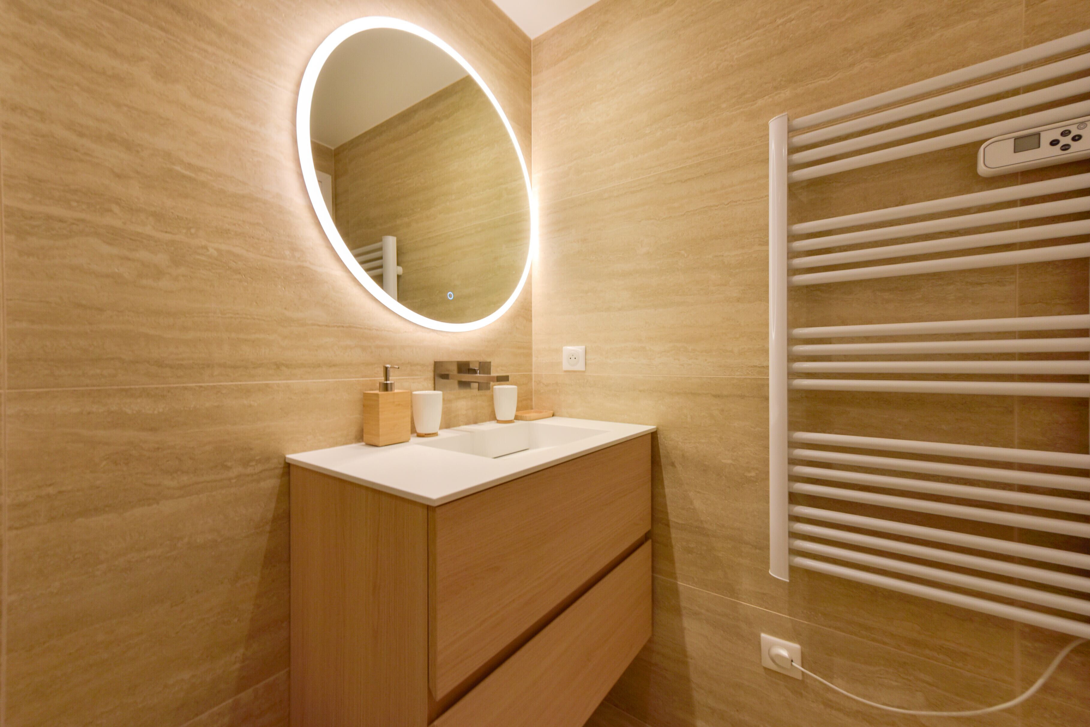 A modern bathroom with a wooden vanity, a mirror with integrated lighting, and a built-in towel rack.