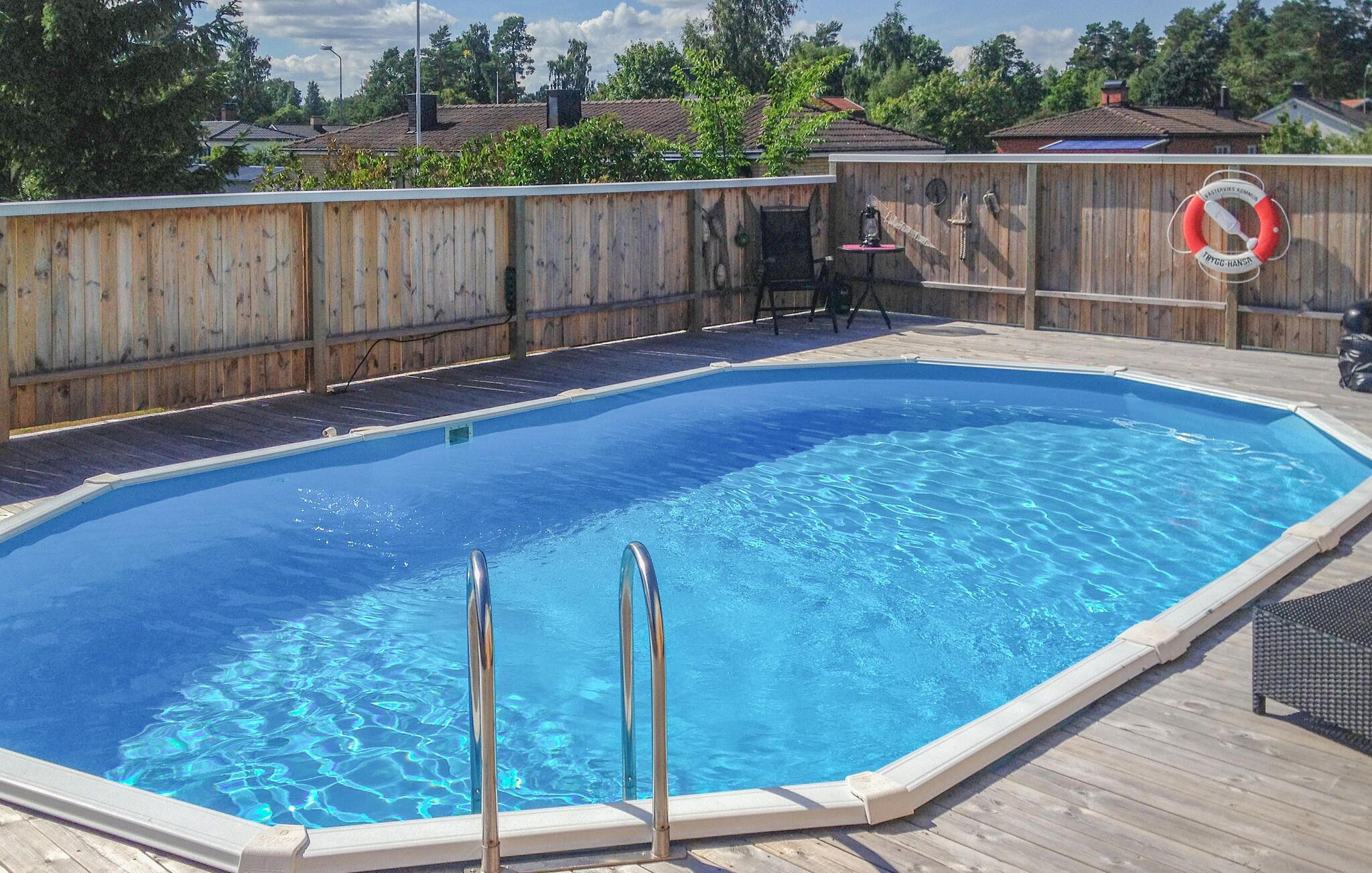 Uma piscina retangular com deck de madeira e um salva-vidas na parede.