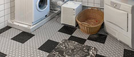 A laundry room with a washing machine, dryer, and a wicker basket on a checkered floor.