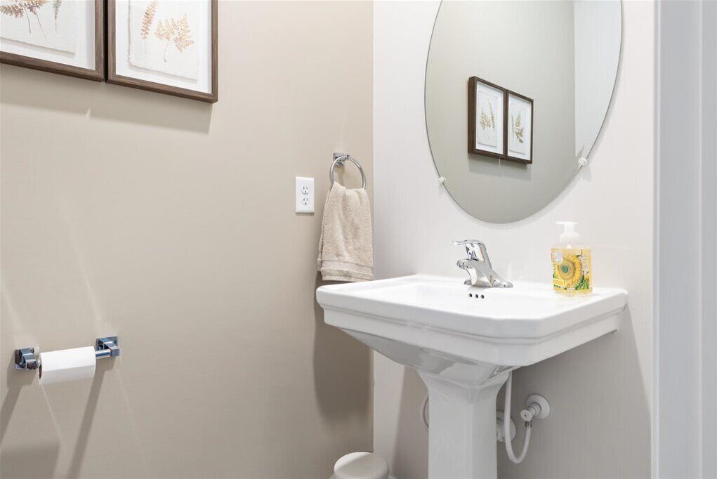 Un bagno con un lavandino bianco, uno specchio e stampe botaniche incorniciate alle pareti.