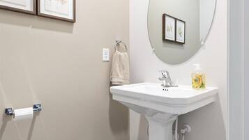 Un bagno con un lavandino bianco, uno specchio e stampe botaniche incorniciate alle pareti.