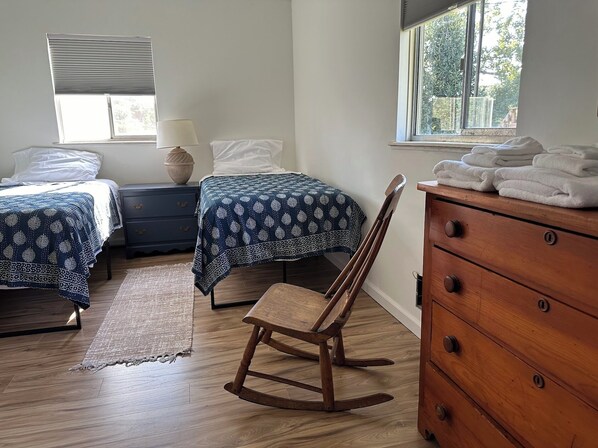 A bedroom with two beds, a rocking chair, a wooden dresser, and a window with a view of trees. - Lake Michigan Beach Time - Private Beach on Lake Michigan (Whitehall)