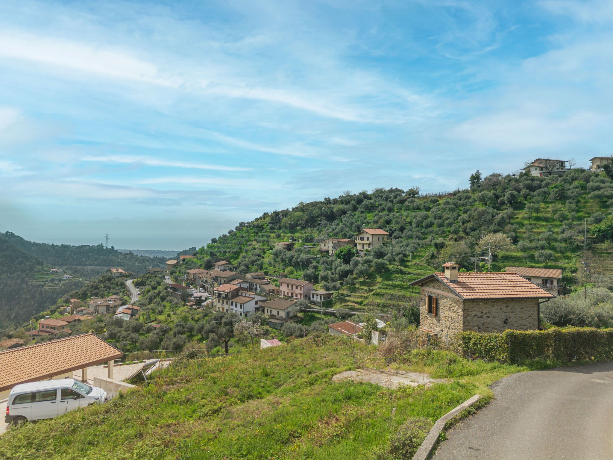 Un pueblo en una ladera con casas de piedra tradicionales, un camino sinuoso y vistas del paisaje distante.
