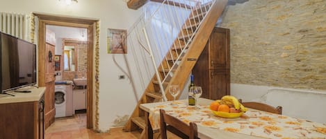Uma cozinha rústica com teto de madeira, parede de pedra e uma mesa de jantar com uma tigela de frutas e copos de vinho.
