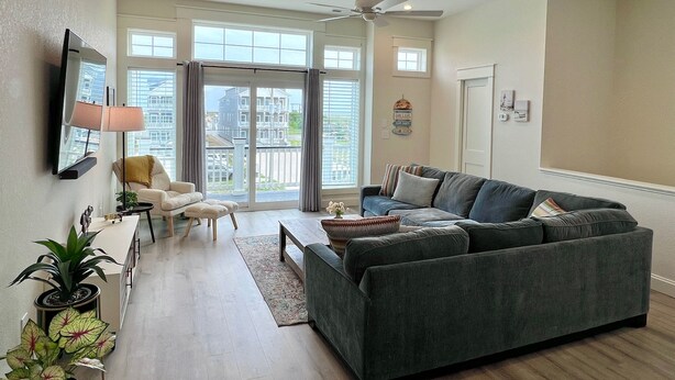 Un salon avec un canapé gris, un fauteuil blanc, une table basse et un téléviseur fixé au mur.