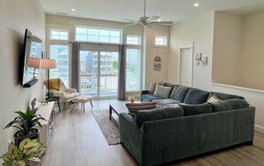 A living room with a grey sofa, a white armchair, a coffee table, and a TV mounted on the wall.