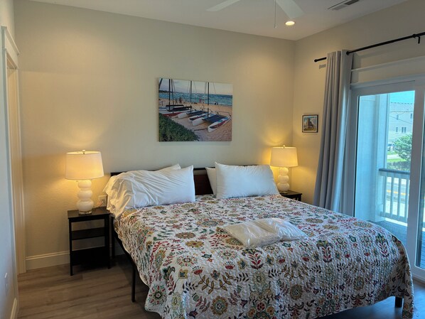 A hotel room with a large bed, two bedside lamps, a painting of a beach scene, and a window with curtains.