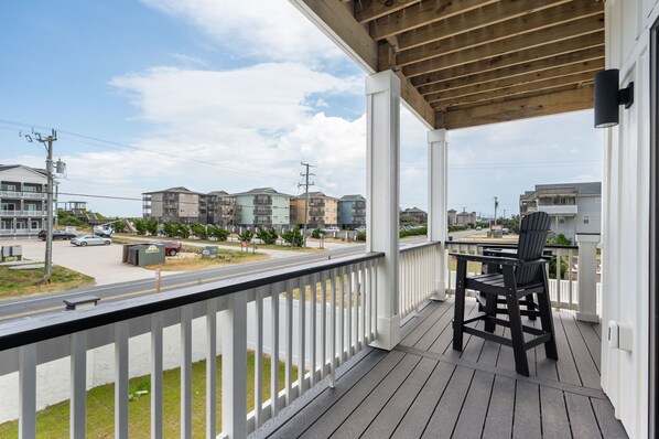 A wooden deck with a chair, overlooking a street with multi-story buildings and parked cars.