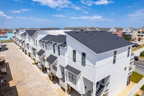 A row of modern, white townhouses with dark roofs, featuring balconies and a clear view of the surrounding neighborhood.
