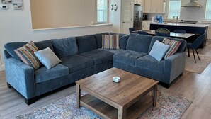 Un salon moderne avec un canapé d’angle, une table basse et une cuisine en arrière-plan.