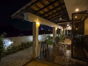 An outdoor patio area with a wooden deck, seating, and a view of the city skyline at night. - Bangsar Private Pool Villa Kuala Lumpur (Kuala Lumpur)