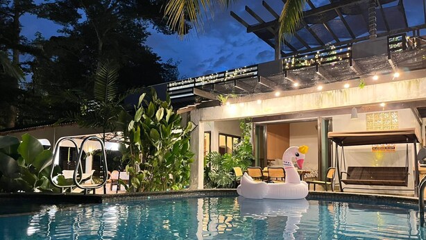 A swimming pool with a swan float, surrounded by lush greenery and a covered area with seating. - Bangsar Private Pool Villa Kuala Lumpur (Kuala Lumpur)