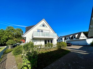 A two-story house with a balcony, surrounded by greenery and a paved driveway. - Haus Sanddorn - Geräumige Ferienwohnung Absoluter Strandnähe - Haus Sanddorn Fewo 07 (Mönchgut)