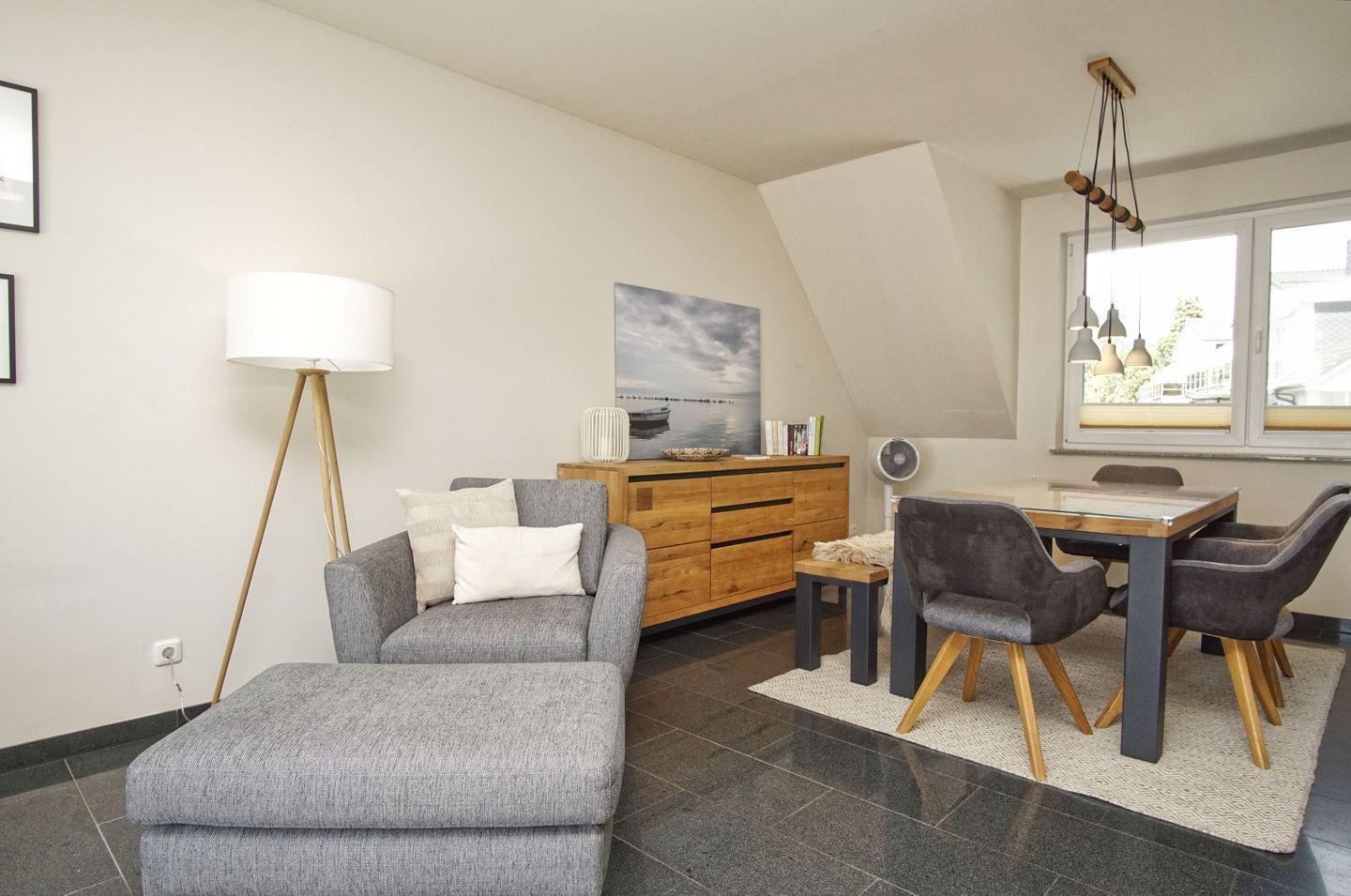 Una sala de estar moderna con un sofá gris, un aparador de madera, una mesa de comedor con sillas y un ventanal con vistas.