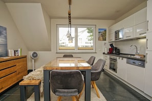 Una cocina moderna con armarios blancos, una mesa de comedor con sillas, un ventilador y un ventanal con vistas a edificios.