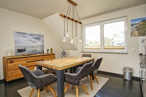 Una cocina moderna con una mesa de comedor de madera, sillas tapizadas en gris, un armario de madera y un ventanal con vistas al mar.