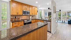 A modern kitchen with wooden cabinets, granite countertops, and stainless steel appliances. - Beautiful Upstairs Corner Cottage - Ocean view from Balcony NCV B2 (Oceanside)