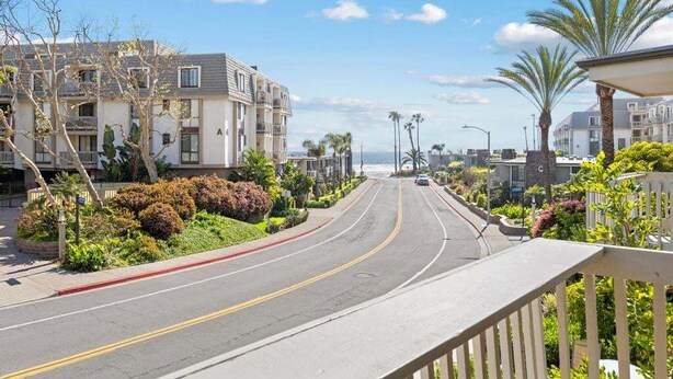 A coastal street with residential buildings, a clear sky, and a view of the ocean. - Beautiful Upstairs Corner Cottage - Ocean view from Balcony NCV B2 (Oceanside)