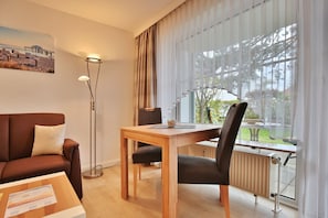 A modern hotel room with a wooden desk, a brown leather sofa, a black chair, and a large window with sheer curtains.