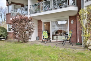 A two-story building with a balcony, a dining area with chairs and a table, and a large window.