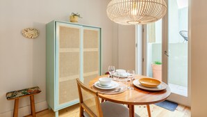 A dining area with a round table set for four, a tall cabinet with a woven front, and a hanging light fixture. - D&S -JB Apartments - A (Oporto)