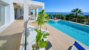 Ein moderner Poolbereich mit freiem Blick auf den Ozean, umgeben von üppiger Bepflanzung und einer Holzterrasse.