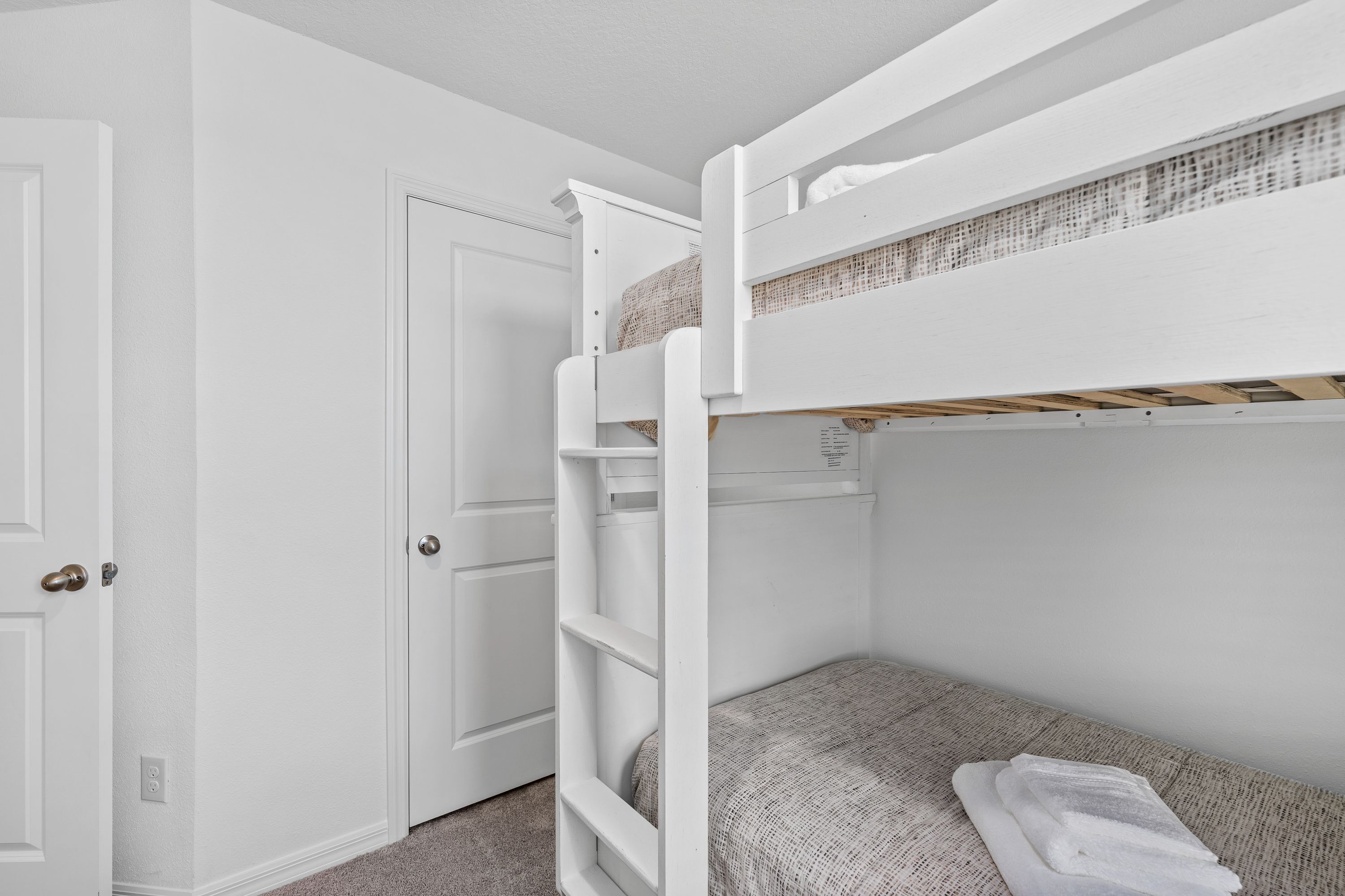Un lit superposé avec une échelle, une porte et une petite table de chevet.