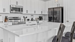 A modern kitchen with white cabinetry, stainless steel appliances, and a central island with bar seating.