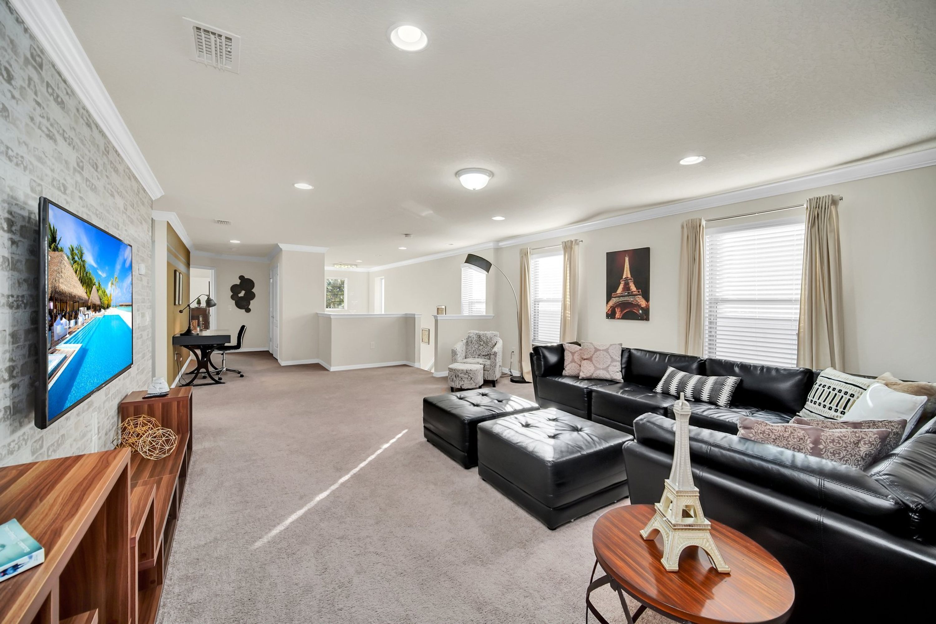 A modern living room with a black leather sofa, a wooden coffee table, and a TV mounted on the wall.