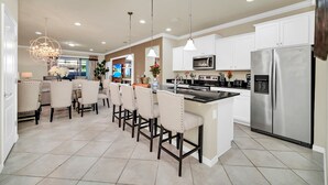 A modern kitchen with white cabinets, a stainless steel refrigerator, and a dining area with beige chairs.