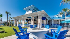 An outdoor seating area with blue Adirondack chairs, a circular fire pit, and a covered patio with tables and umbrellas. - Amazing Modern Home Pool Spa Game Room Wi101 (Davenport)