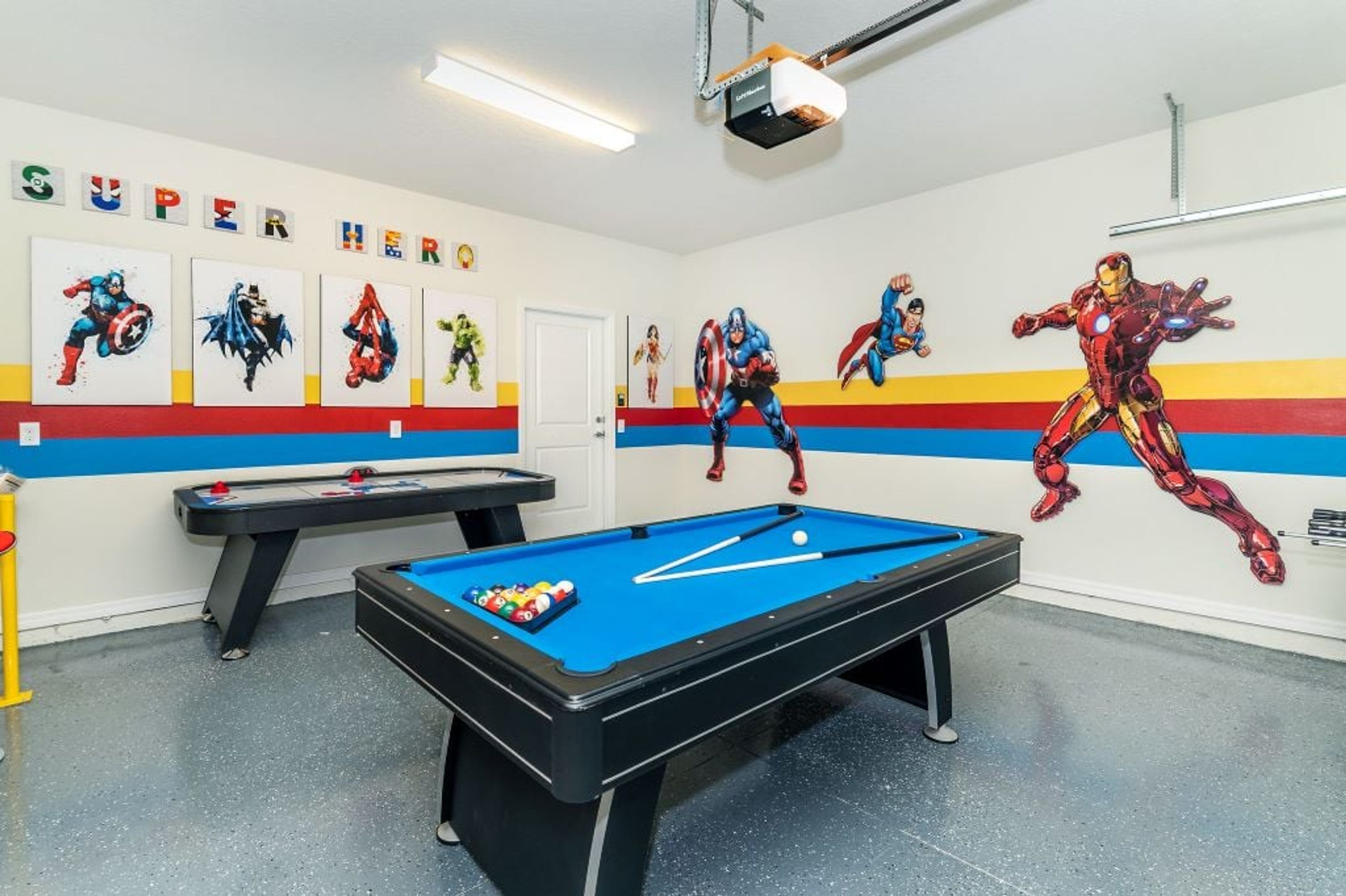 A pool table in a room with superhero-themed wall art and a projector.