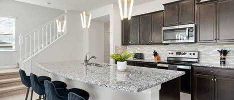A modern kitchen with dark wood cabinets, a granite island with bar stools, stainless steel appliances, and pendant lighting.