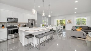 Una cocina moderna con armarios blancos, electrodomésticos de acero inoxidable y una isla central con taburetes de bar.