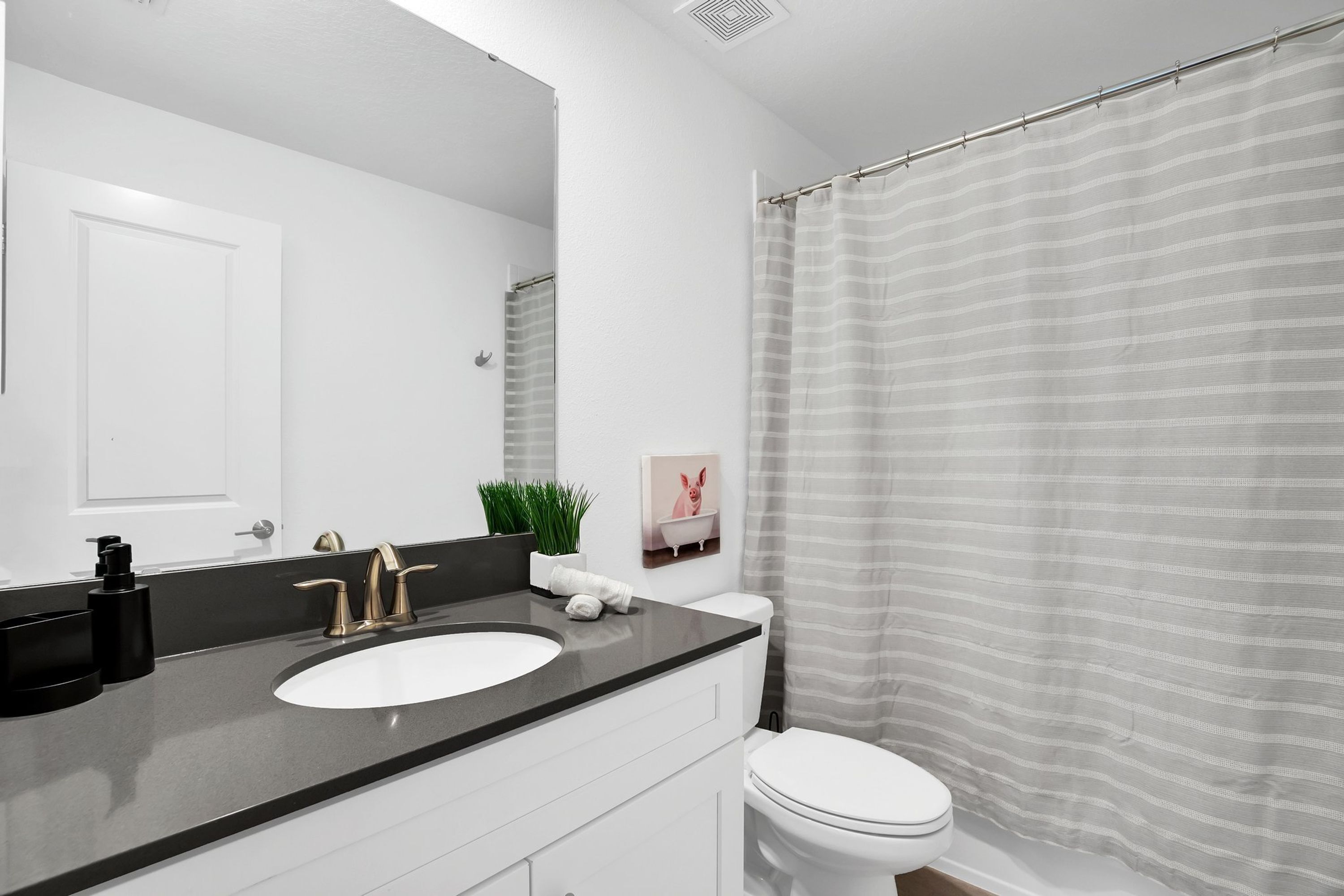 A modern bathroom with a black countertop sink, white toilet, and a shower curtain.