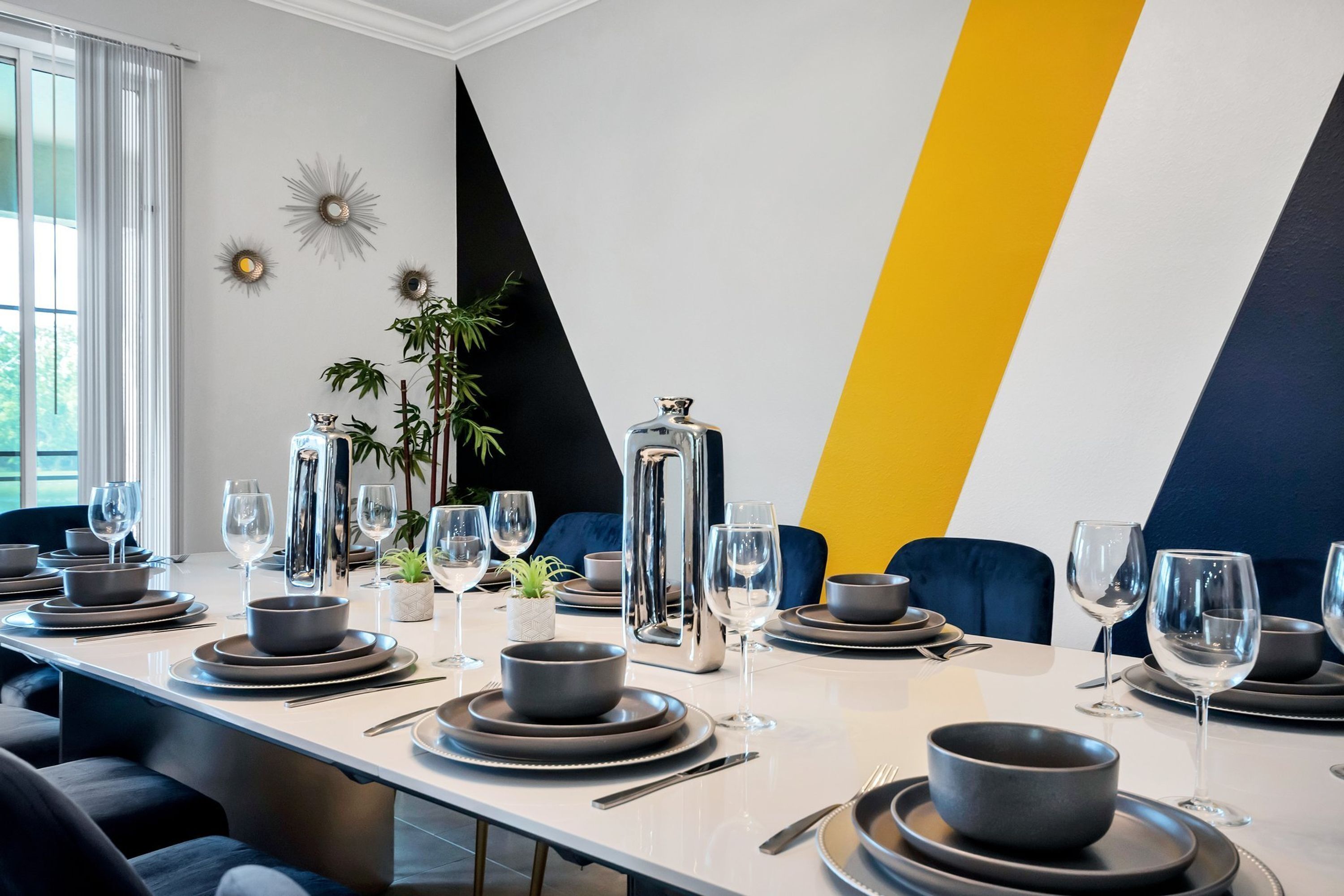 A dining area with a long table set for a meal, featuring modern decor and a geometric wall design.