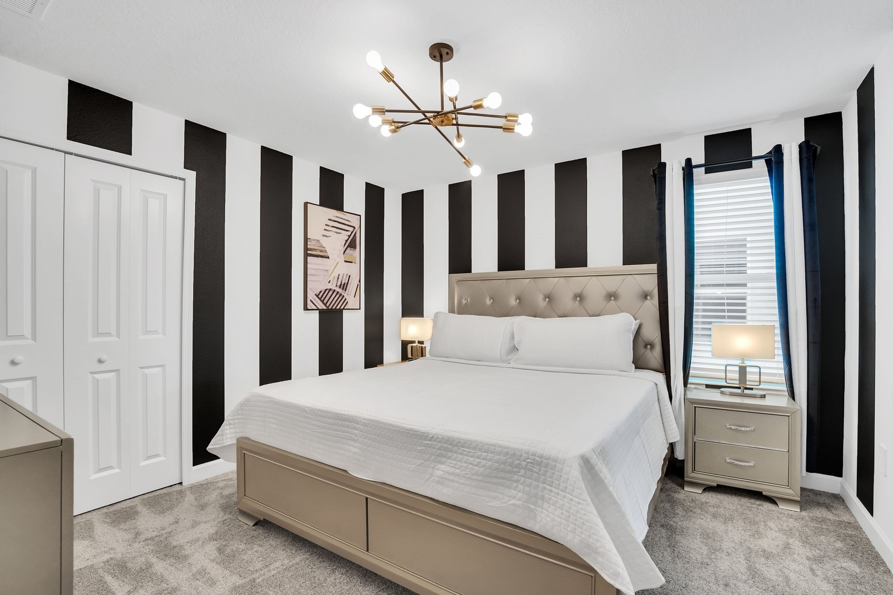 A bedroom with a bed, bedside tables, a nightstand, a ceiling light fixture, and a window with curtains.