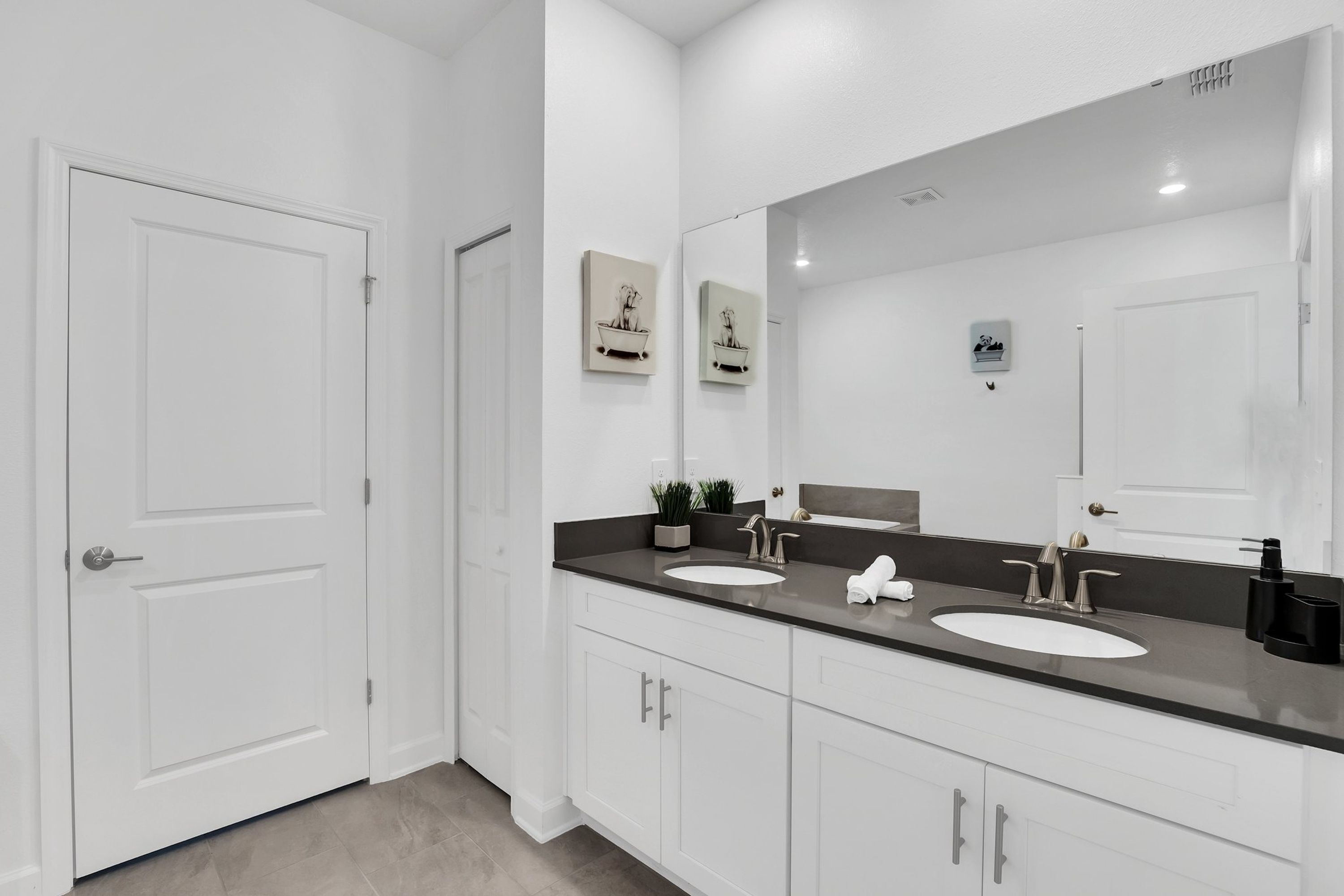 A modern bathroom with two sinks, a large mirror, and white cabinetry.