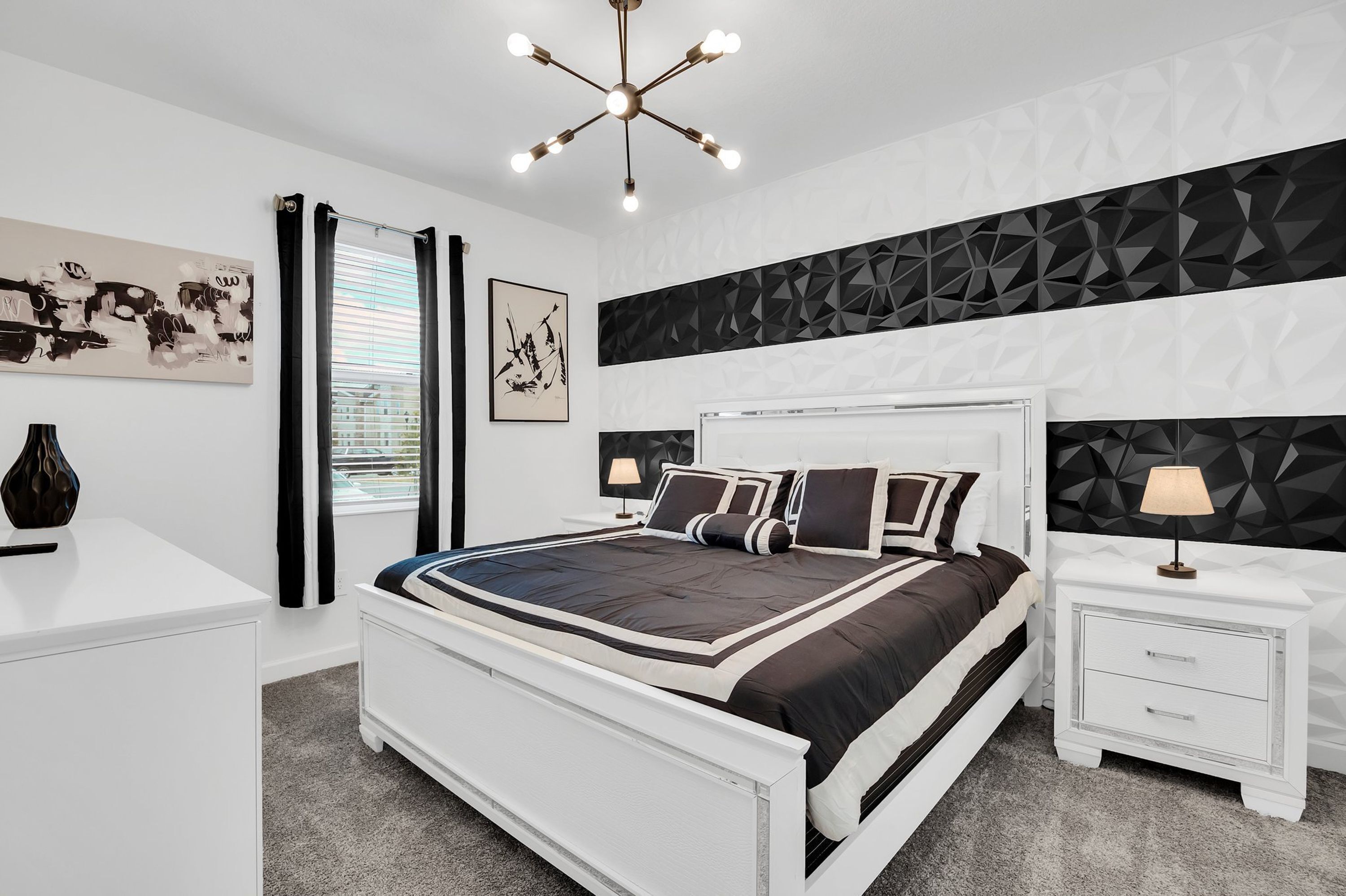 Ein modernes Schlafzimmer mit einem weißen Bett, schwarz-weißer Bettwäsche, einem Kopfteil mit geometrischem Muster und einem Nachttisch mit Lampe.
