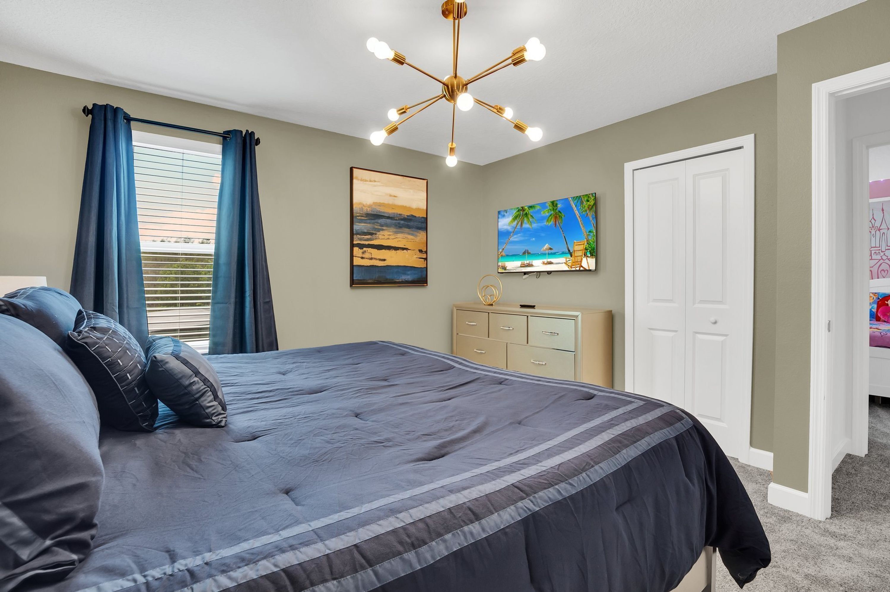 A bedroom with a large bed, a ceiling light fixture, a dresser, and a door.