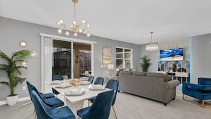 A modern living room with a grey sofa, a dining table with blue chairs, and a chandelier.
