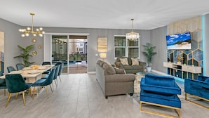 A modern living room with a grey sofa, blue velvet chairs, and a dining area with a table and chairs.