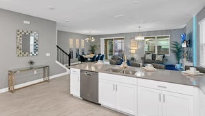 A modern kitchen with a central island, white cabinetry, and a dishwasher. There is a dining area with blue chairs and a chandelier.