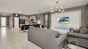 A modern living room with a grey sectional sofa, a small round table, and a TV mounted on the wall. - Magical Family Home 8min-disneyworld Pool Spa Sleeps 22 Stl103 (Kissimmee)