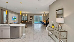 A modern kitchen with a central island, a dining area with a glass table, and a living room with a sofa and TV. - Disney Decorated Home 8min to Disneyworld Pool Spa Sleeps 22 Stl104 (Kissimmee)